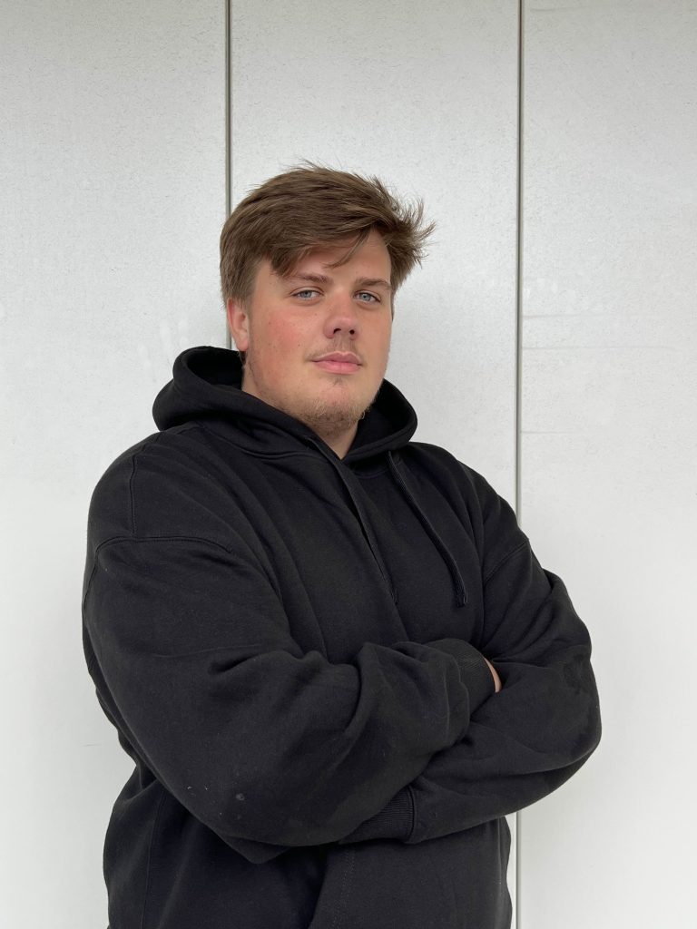 un homme en pull noir les bras croisés